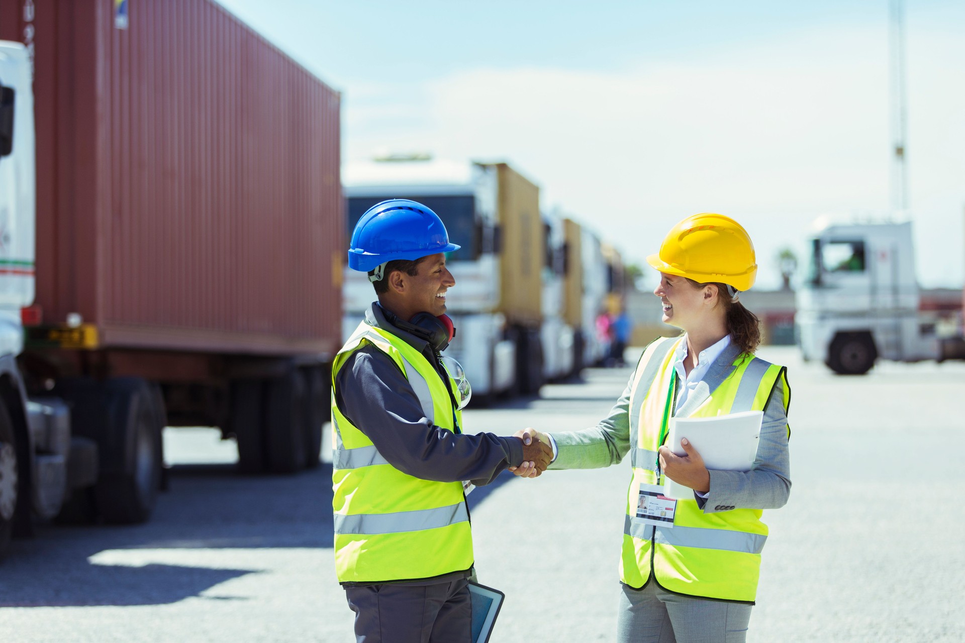 Arbeiter und Geschäftsfrau schütteln Hände in der Nähe von Lastwagen und Frachtcontainern